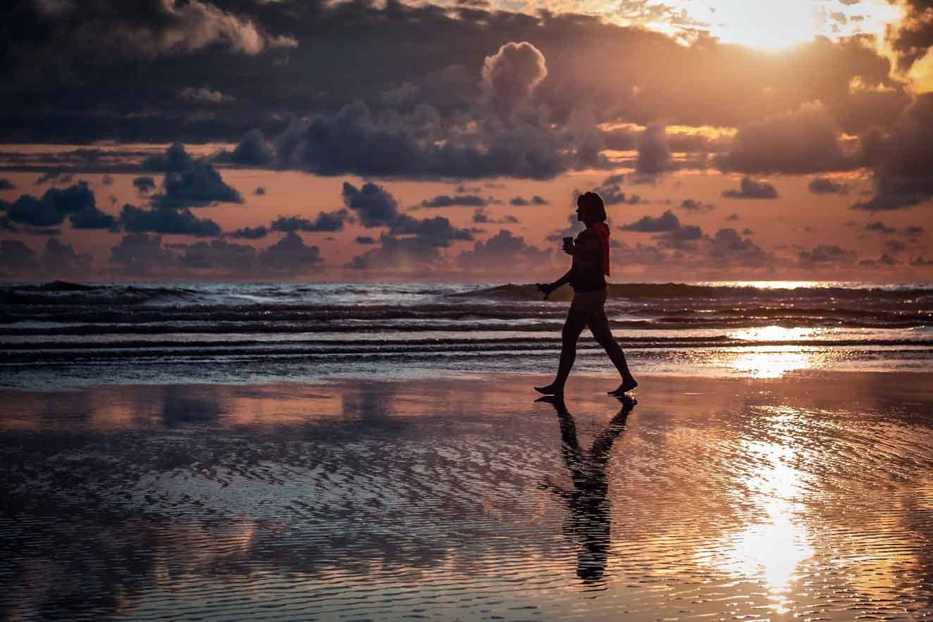 Woman practicing Self-Care, walking on beach at sunrise. Photo taken in 2022.