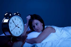 Girl in bed not able to sleep with a clock in the foreground