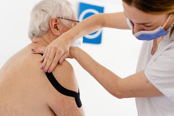 A therapist puts neuromuscular tape on a client’s shoulder