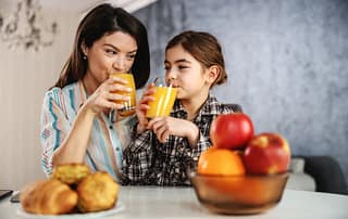 Mother And Daughter Having A Healthy Breakfast. They Are Drinking Orange Juice.