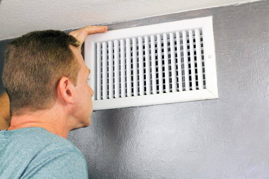 Man looking closely at white air vent in gray wall