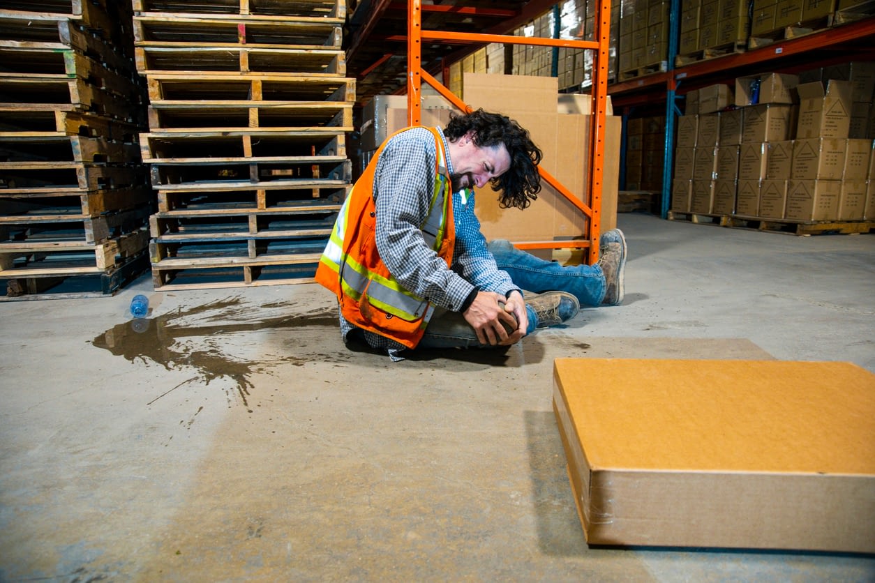 injured man sitting on warehouse floor holding his knee