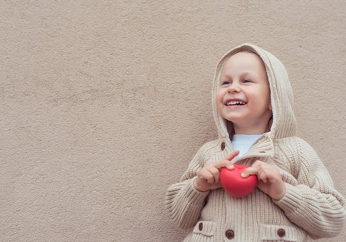 Joyful young boy holds red heart.