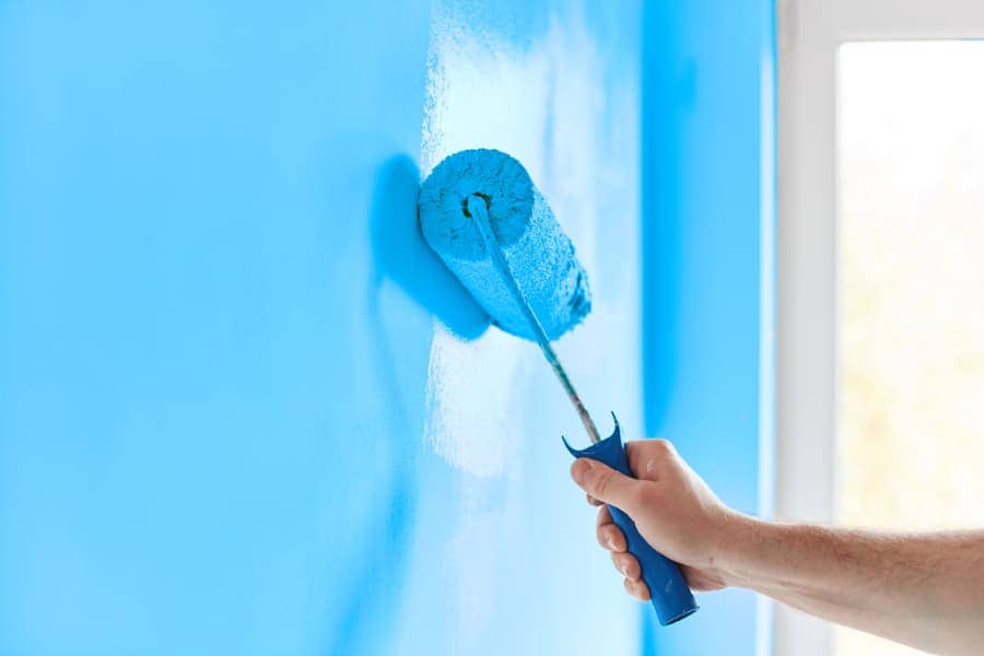 A paint roller applies blue paint to a wall.
