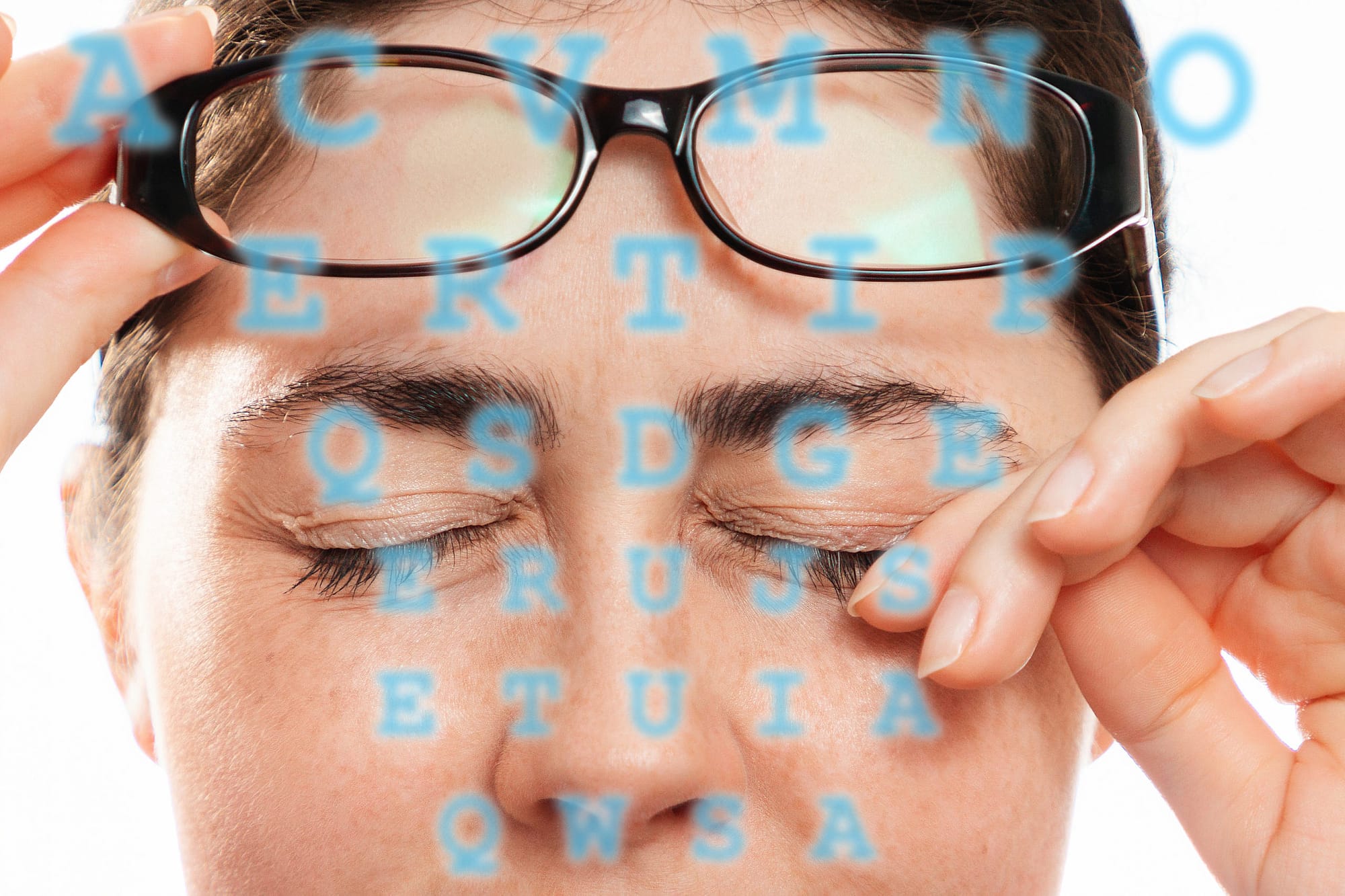Close-up of woman’s face scratches her painful eyes, taking off her glasses. Blue letters in the foreground. The concept of unhealthy eyes and vision