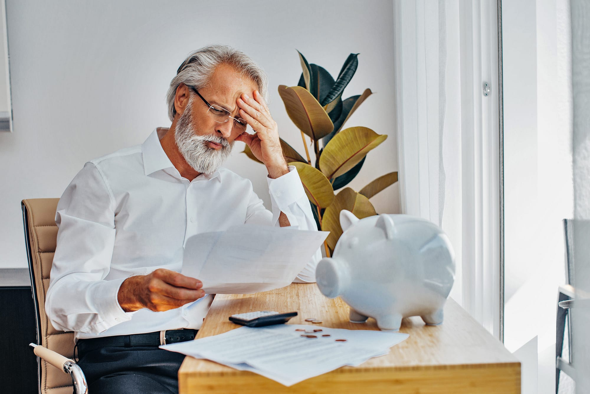 Portrait of a senior white hair man at home desk worried about money, contracts and paying bills or loans