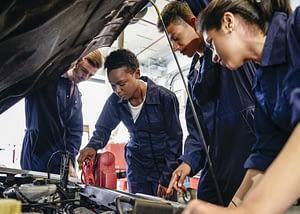 Group Of Student Mechanics Working On Car Engine With Hood Up