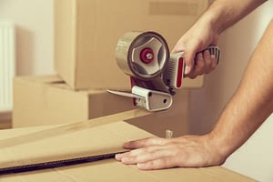 A man uses a tape dispenser to seal a packing box