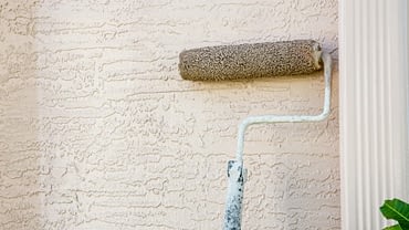 Paint roller being used on stucco wall