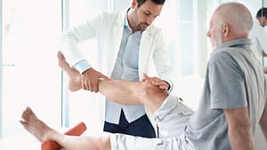 elderly man sitting on exam table with male doctor examining his knee