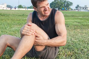 man sitting on ground holding his left thigh and knee