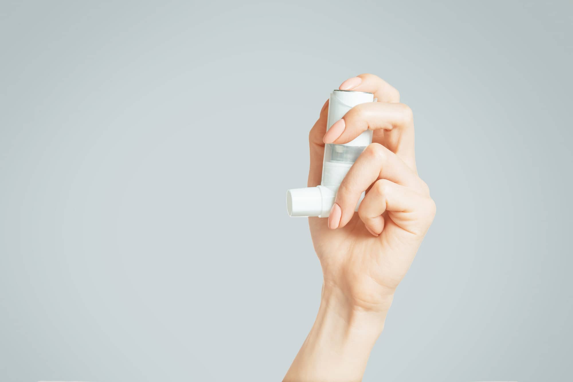 Female hand holding a medical asthma inhaler.