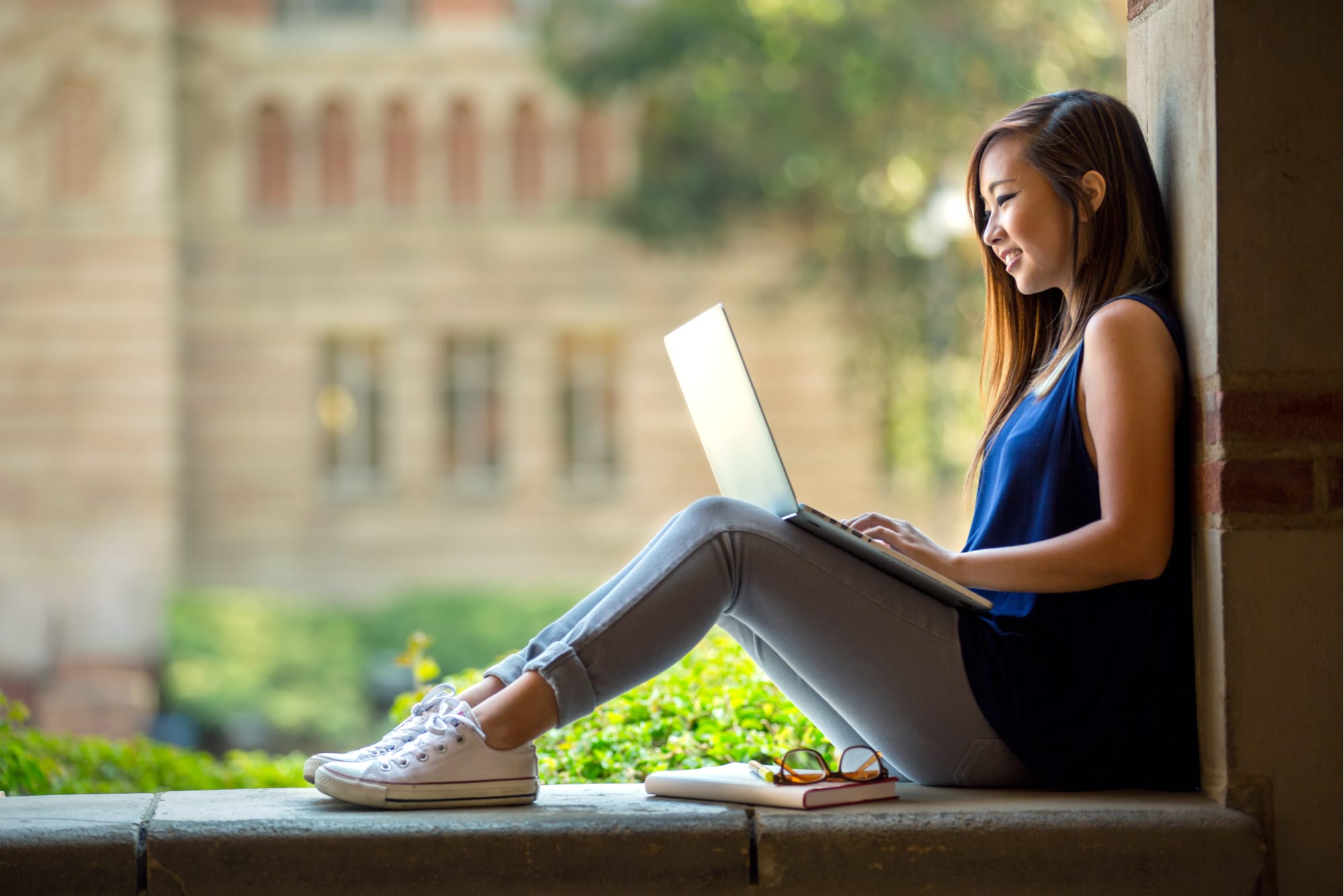 Smiling student on laptop studying outdoors