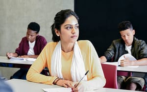 Three students sitting at tables in classroom for English course 
