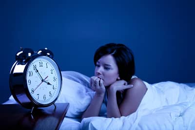 woman in bed with insomnia staring at alarm clock