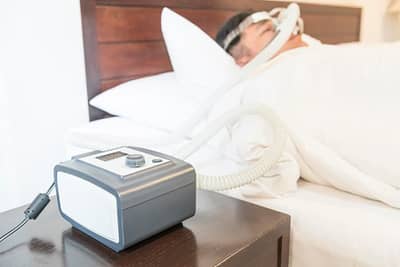 cpap machine on nightstand and a man in bed sleeping with mask on