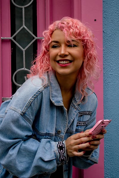 woman with pink hair laughing and texting on her phone