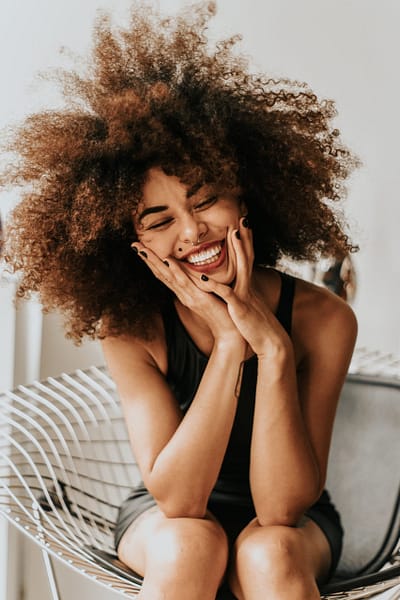 woman with natural curly hair sits in a chair and laughs