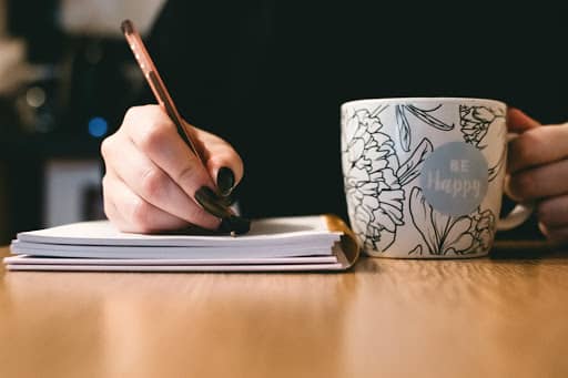Woman writing in notebook while holding a coffee cup