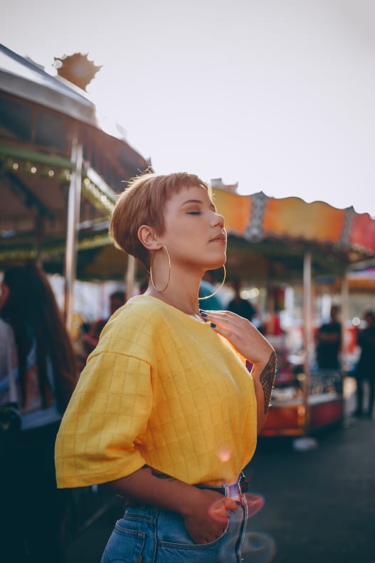 Girl with pixie cut in a yellow top at a carnival.