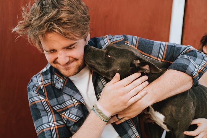 Man in a plaid shirt with messy hair holding a dog.