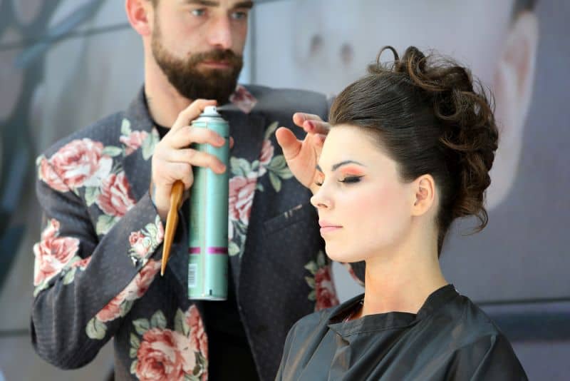 Male hairstylist styling hair with hairspray