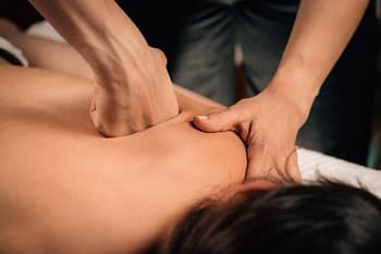 Therapist uses knuckles on back of prone client to provide deep tissue massage