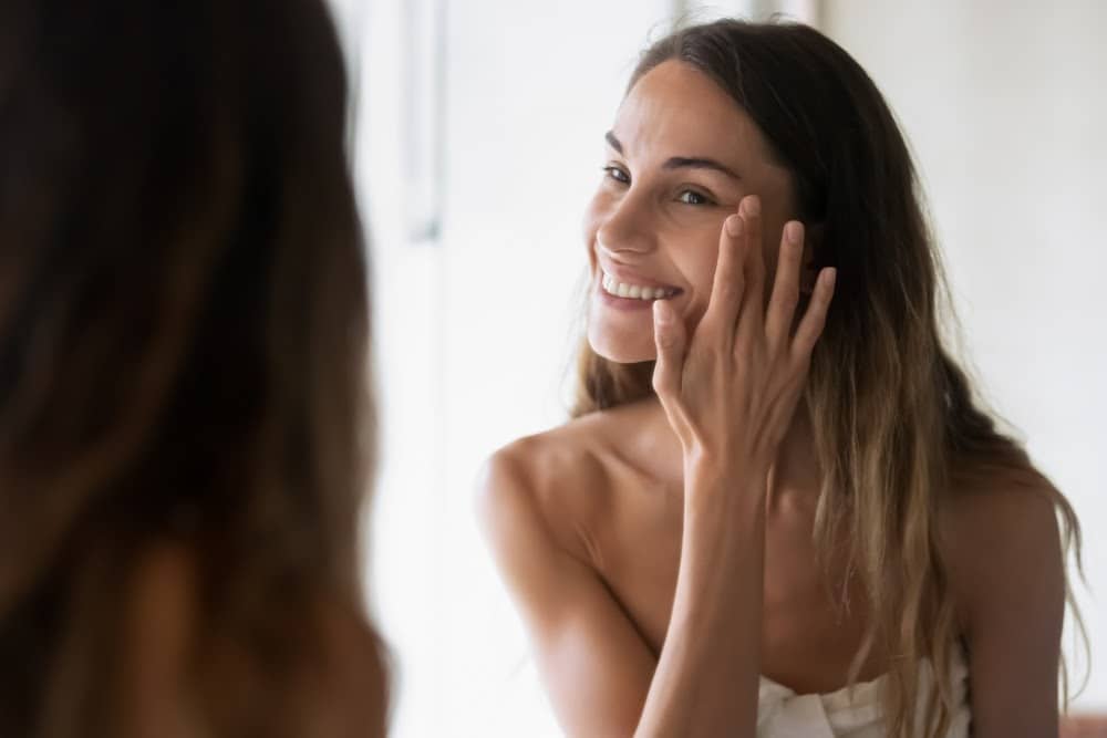 woman looking in the mirror and putting product on her skin