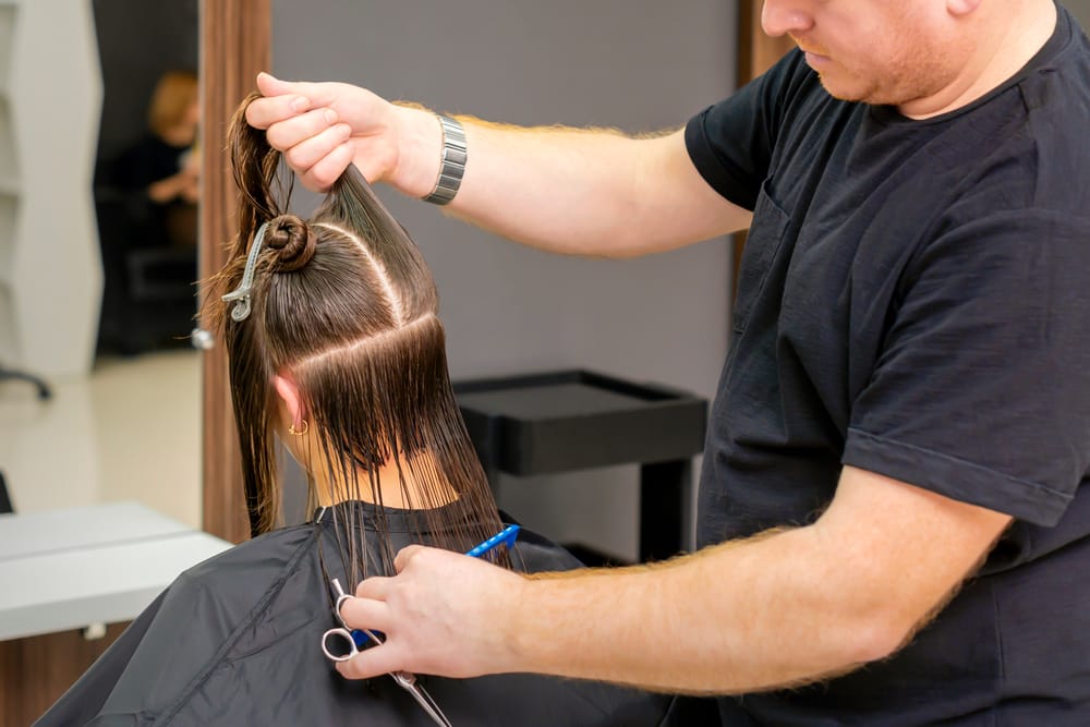 Stylist combing client’s parted hair and holding scissors