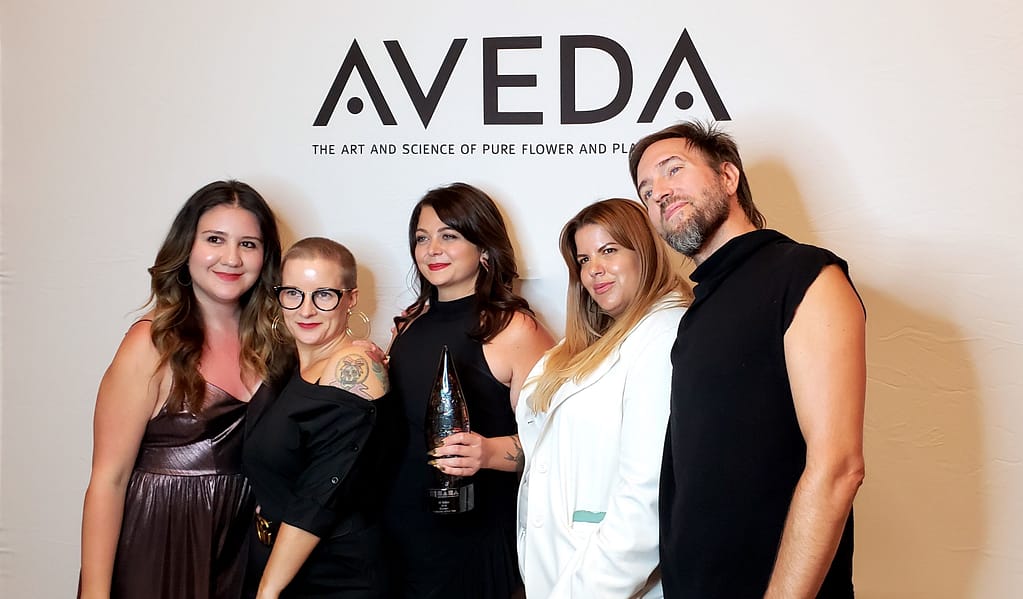 Ali standing with Aveda Institute people in front of Aveda sign