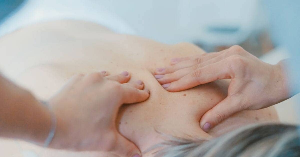 Massage therapist applies manual technique with both hands to client
