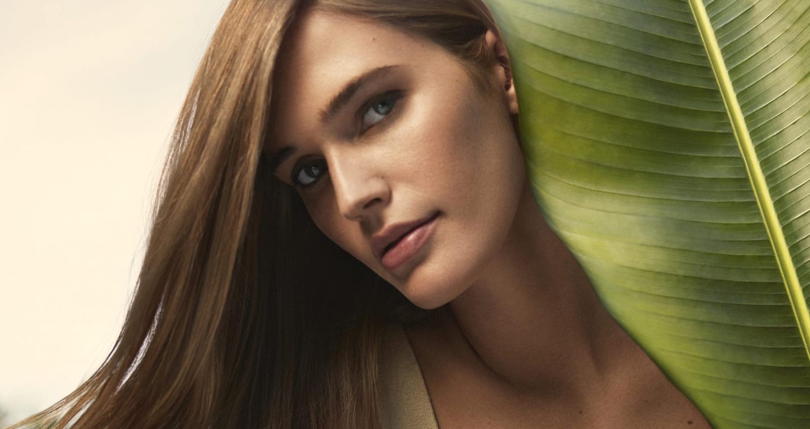 Woman peering around large leaf with hair and makeup done