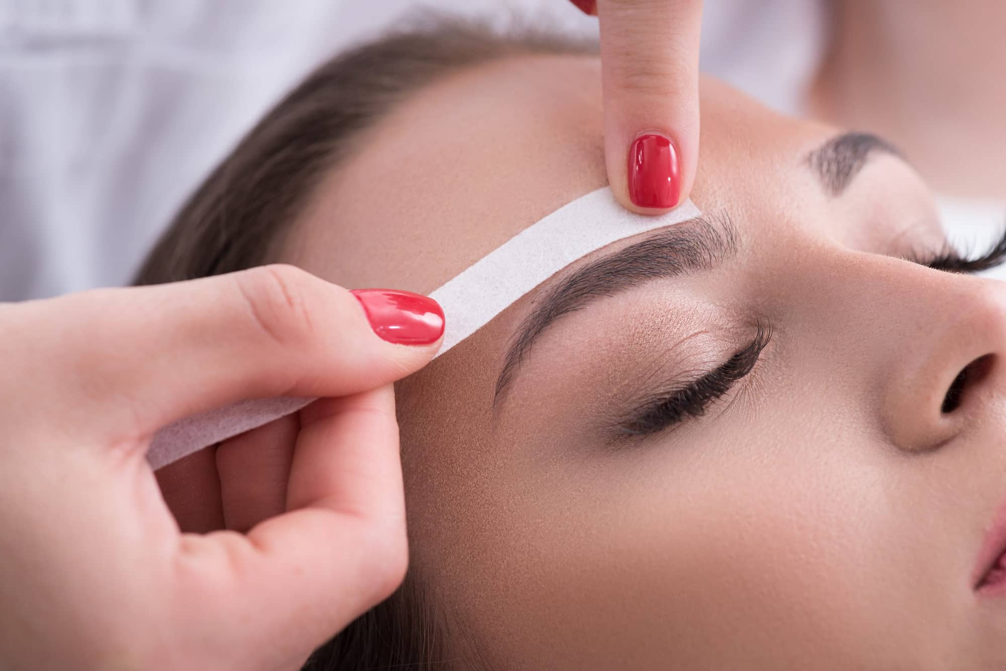 Esthetician shaping client’s eyebrows during salon appointment