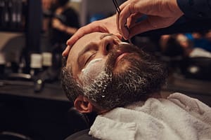 Barber using straight razor to shave man’s beard