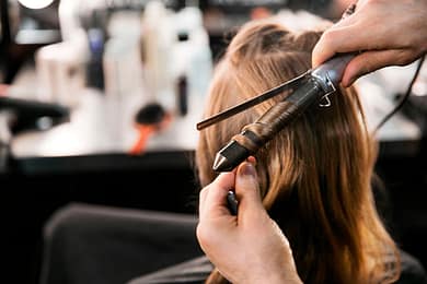 stylist curling a woman's hair with a curling iron