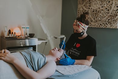 Esthetician using dermaplane on patient’s face with aromatherapy products in background