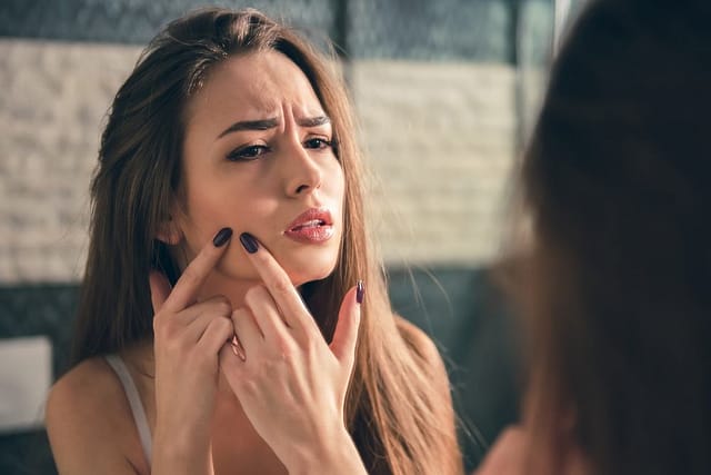 Woman with long brown hair examines a pimple.