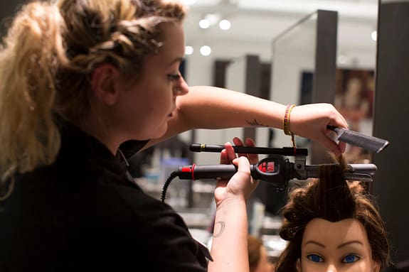 cosmetology student curling a mannequin head's hair