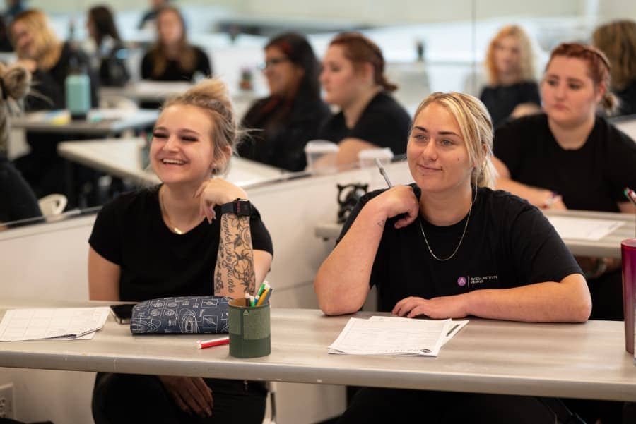 Cosmetology students sitting at desk listening attentively to instructor