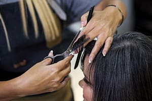 Cosmetology student cutting dark haired woman's hair