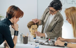 Cosmetology instructor teaching two students using training mannequin