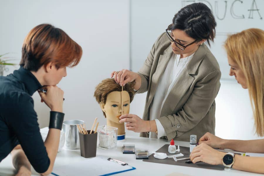 Cosmetology instructor teaching two students using training mannequin