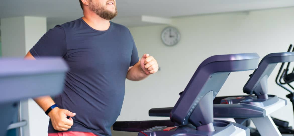 chubby man walking on running track, warming up on gym treadmill.