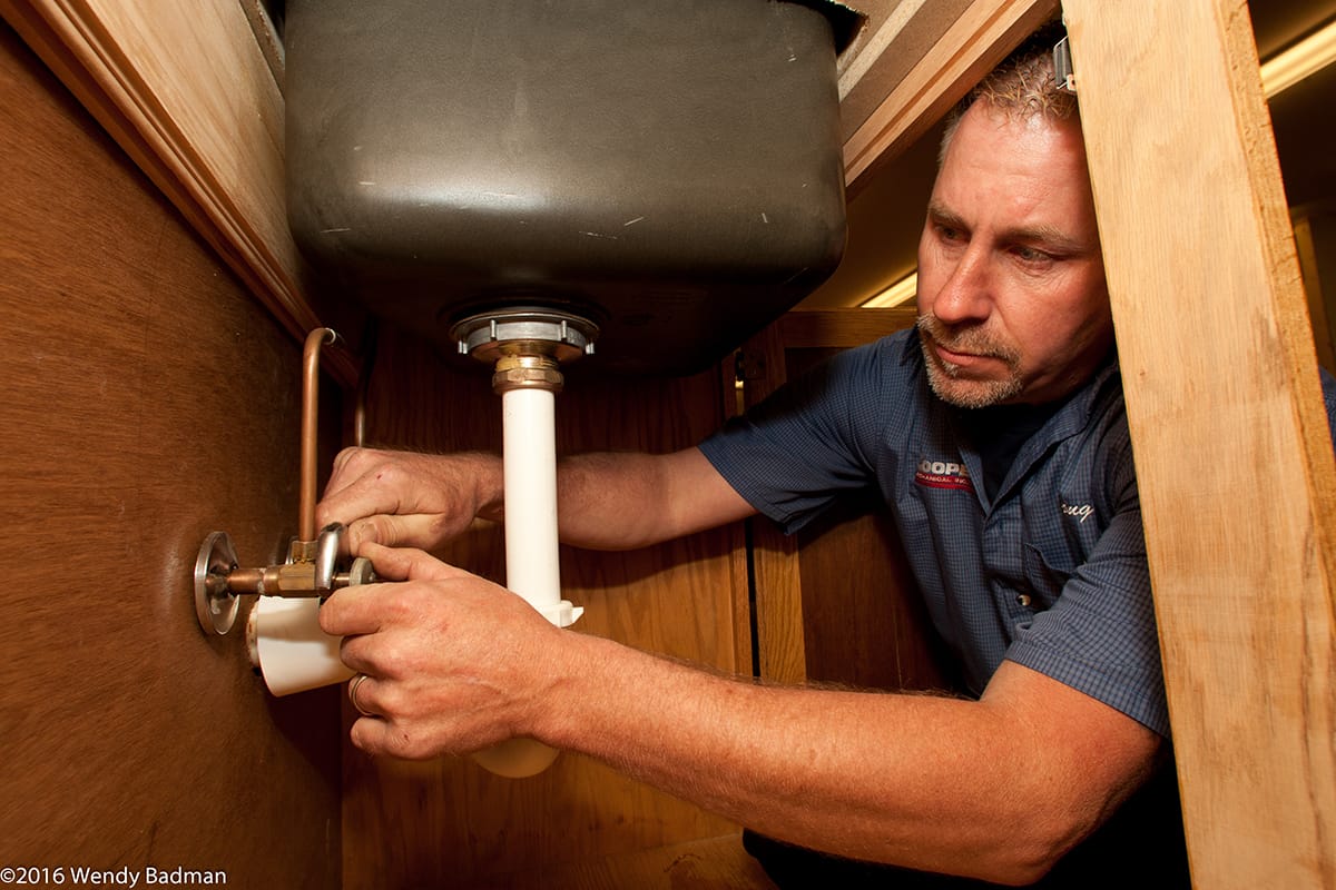 Cooper Mechanical plumbing technician performing plumbing services under sink