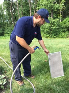 Cooper Mechanical Technician Cleaning Filter In Yard With Hose