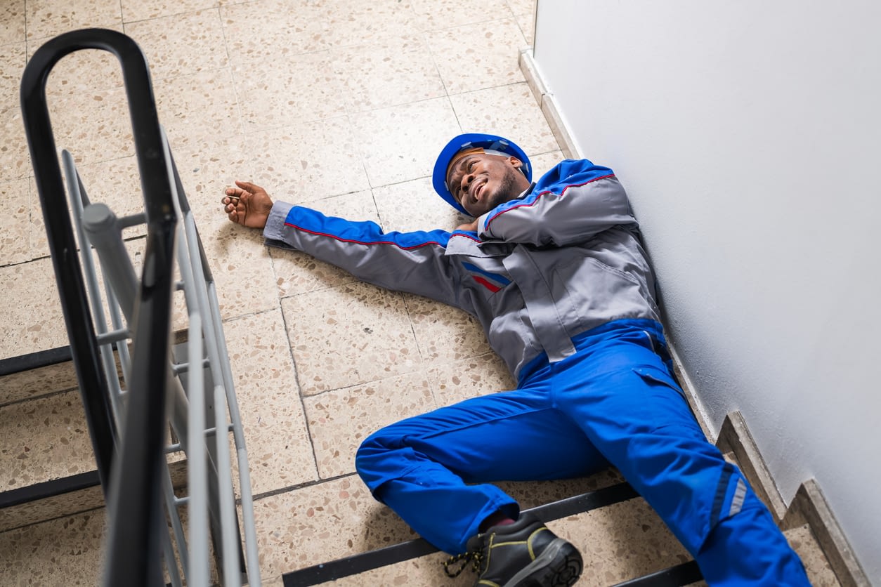 injured man with a blue hard hat on his head laying at the bottom of stairs