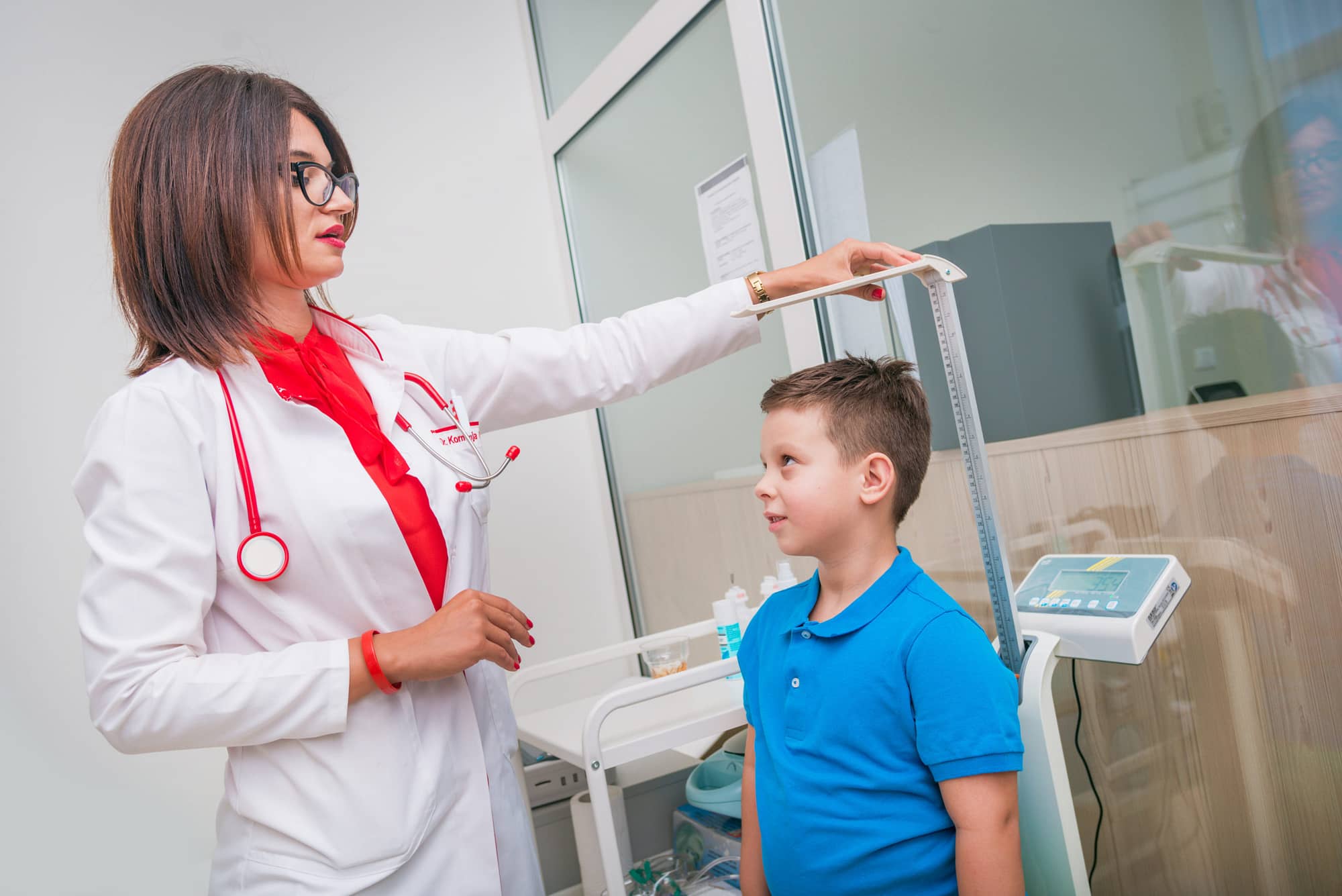 Female doctor measuring the height of little boy in a clinic ( hospital ) while smiling and being gentle.