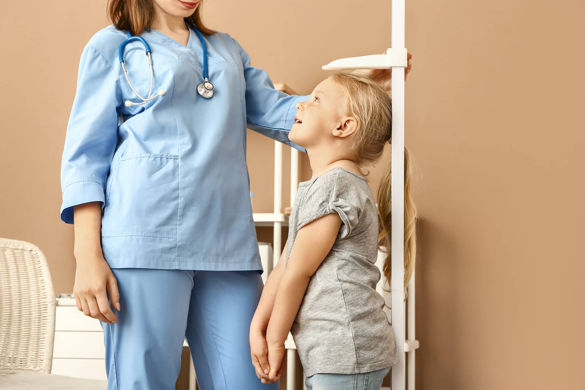 Female nurse measuring height of little girl in hospital