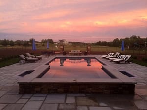 Outdoor Pool Surrounded By Chaise Lounges And Umbrellas At Sunset