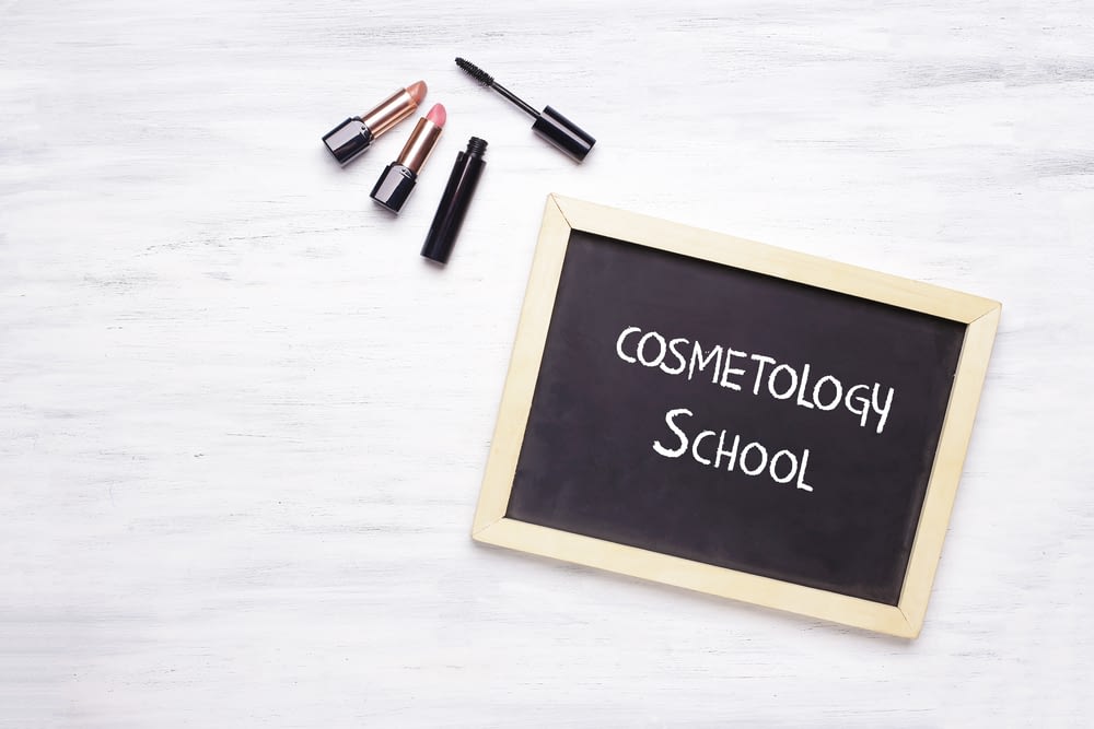 Chalkboard that says "cosmetology school" with makeup surrounding it